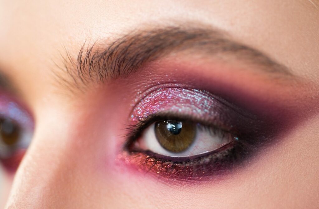 Closeup of a brown eye with beautifully shaped sparkly red, pink, and dark purple eye shadow and black mascara.