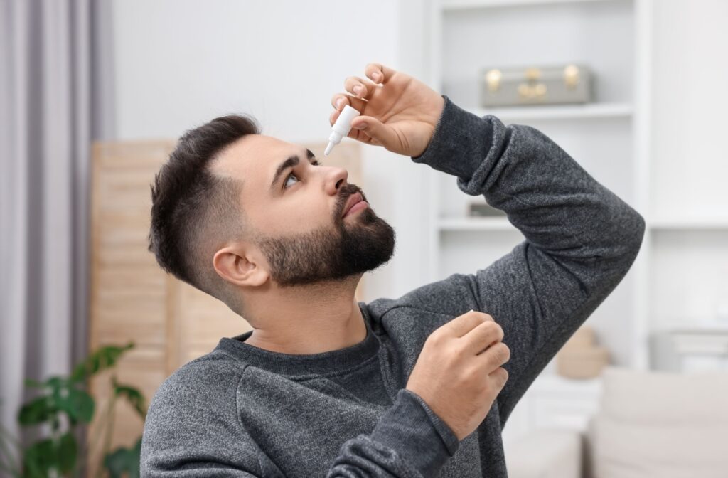 A person tilting their head back while applying eye drops in a home setting.
