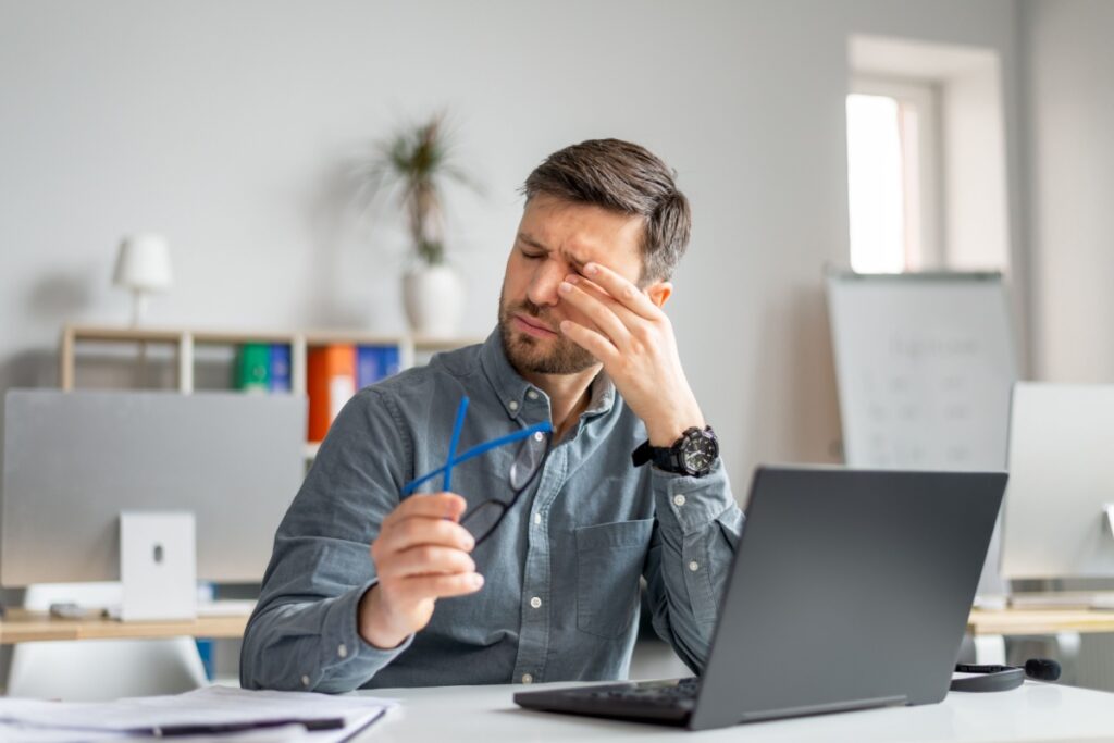 Man rubbing dry eyes at computer.